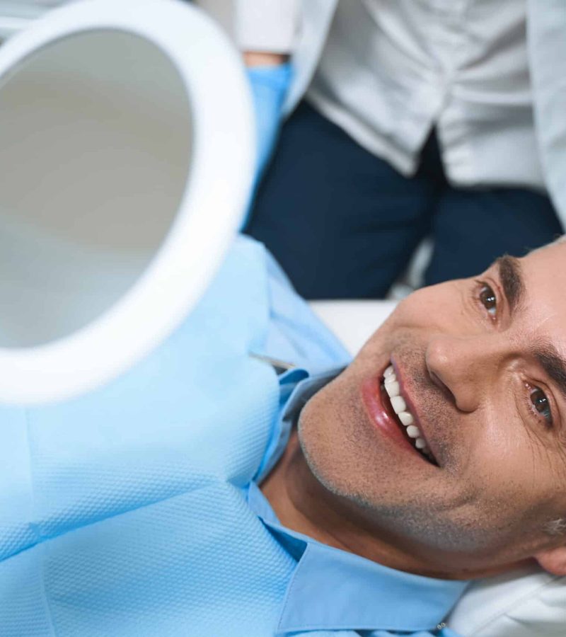 joyful male is lying chair looking into mirror while being delighted with dentist work